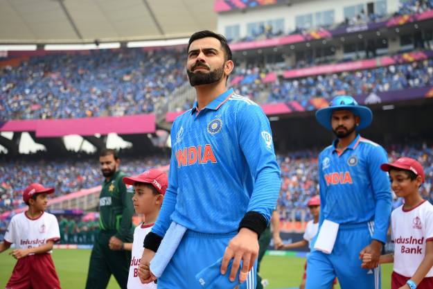 Batter Virat Kohli walks out on to the cricket pitch in a packed stadium 