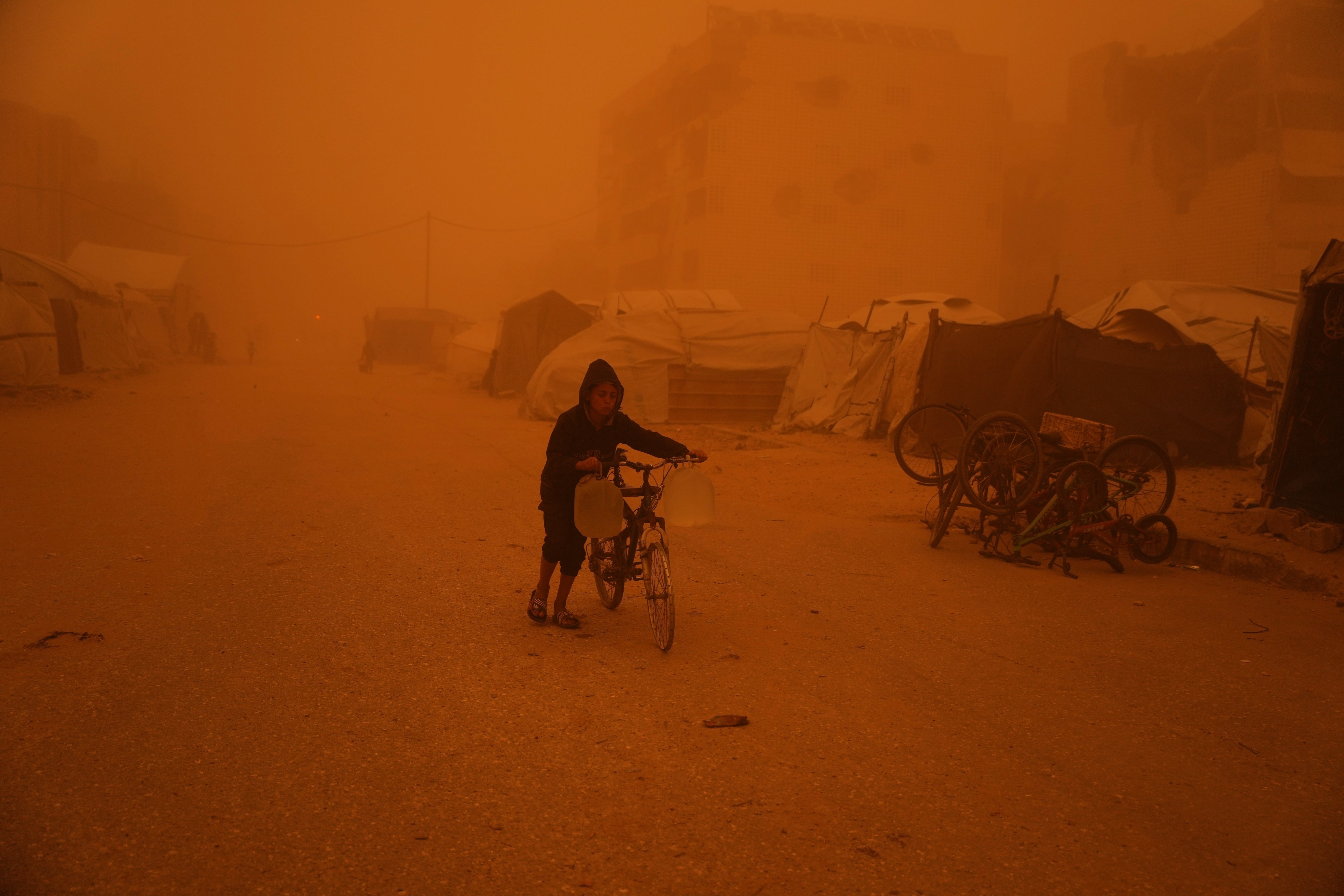 A boy pushes a bicycle carrying jugs of water through a sandstorm in Khan Younis, southern Gaza Strip, March 14, 2026