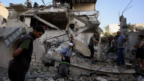 Reuters Palestinians inspect the site of an Israeli strike in Gaza City, northern Gaza (20 August 2025)