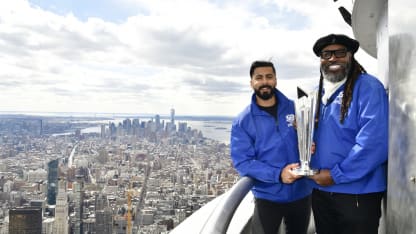 Ali Khan and Chris Gayle with the ICC Men's T20WC Trophy and the view of downtown Manhattan